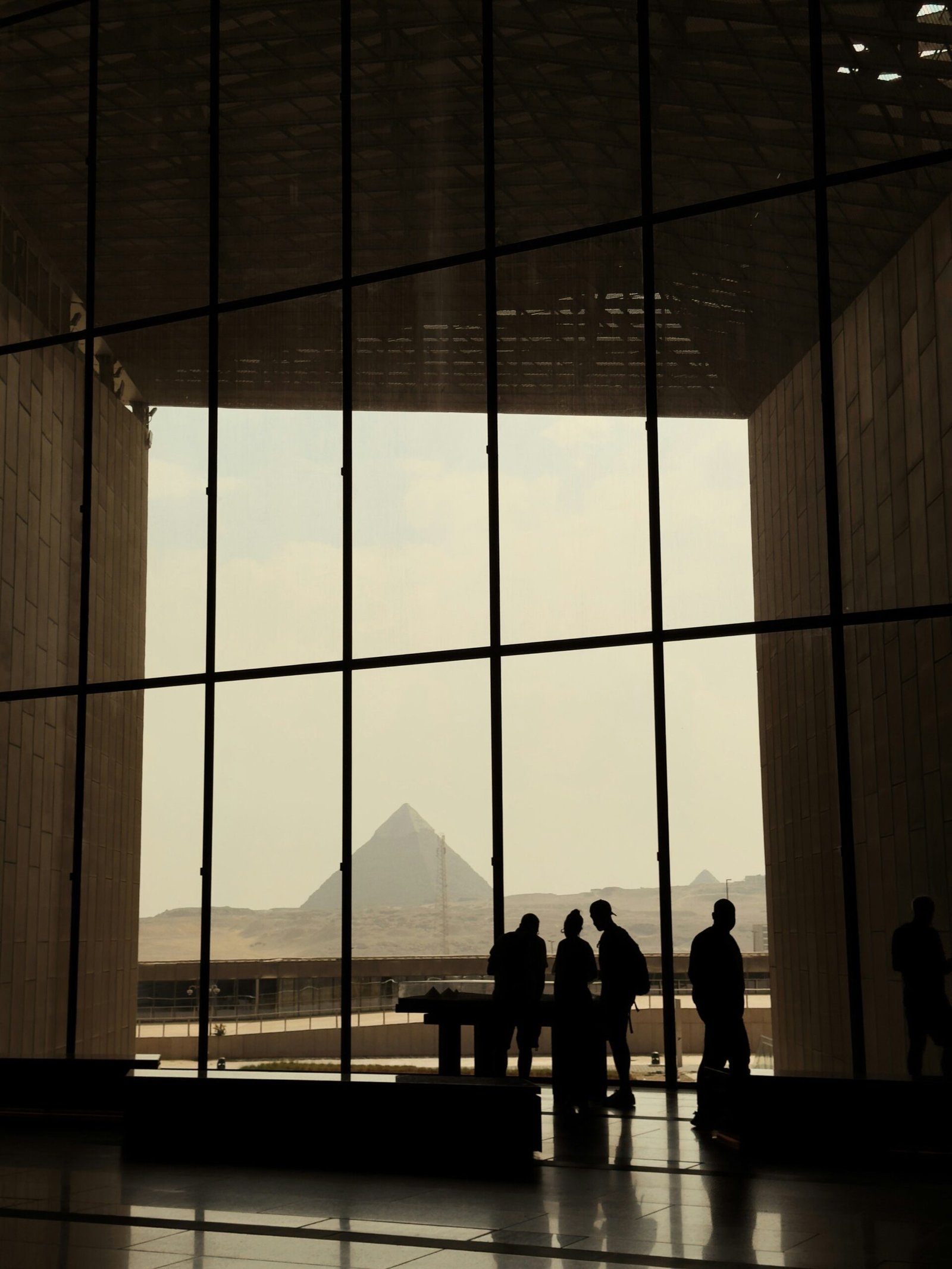 Silhouettes inside a modern building in Cairo with the Pyramids of Giza visible through the large windows.