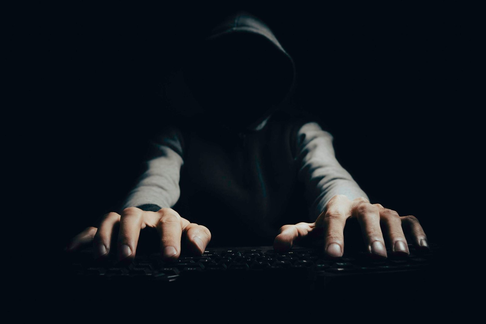 Hands of a hacker typing on a keyboard in a dark room representing cyber attacks and digital breaches