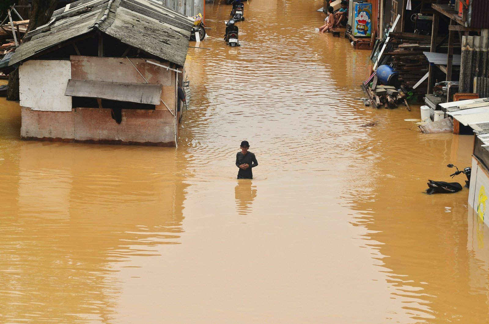 A man walks through deep floodwater in a Jakarta neighborhood after severe rainfall caused widespread damage to homes.