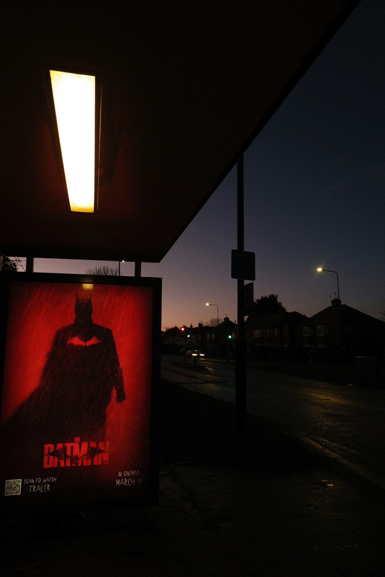 Moody night scene with a red Batman poster at a bus stop promoting The Batman film, matching the dark tone of the sequel news.