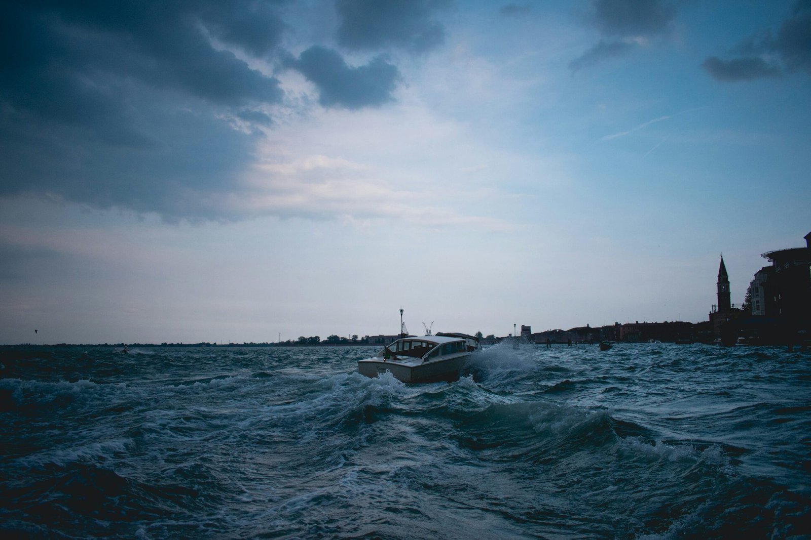 “Boat moving through rough ocean waters under a dark cloudy sky near a distant coastline.”