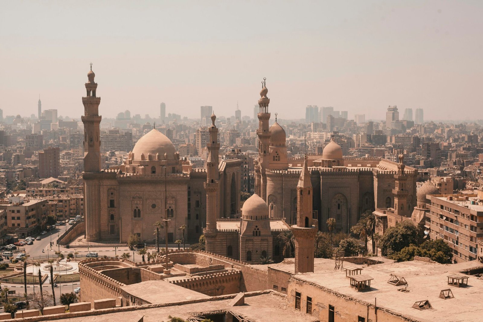 A panoramic view of Cairo showing historic mosques in the foreground and the modern city skyline in the distance.