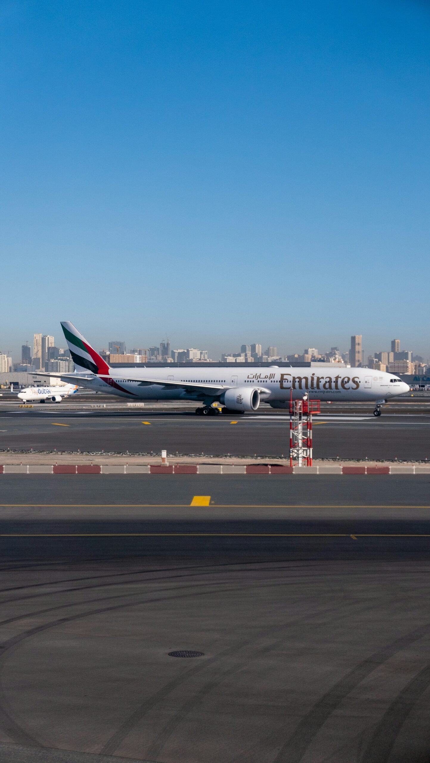An Emirates aircraft taxiing at Dubai International Airport with the city skyline in the background.