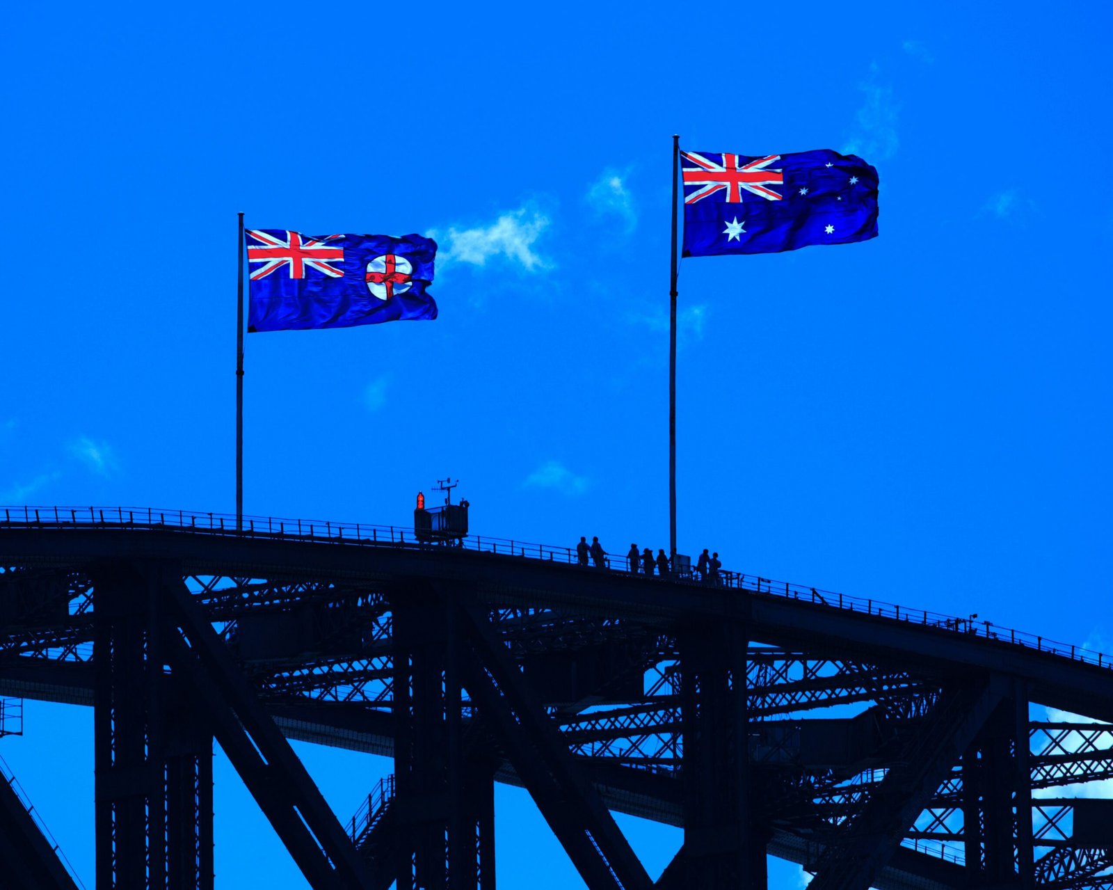 “Australian flags flying over the Sydney Harbour Bridge against a clear blue sky.”