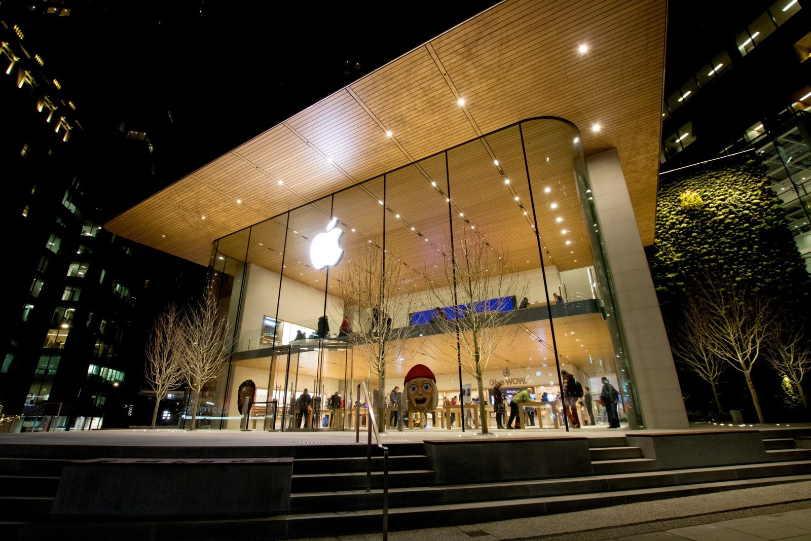 Exterior view of an Apple Store at night with glass walls and the illuminated Apple logo.